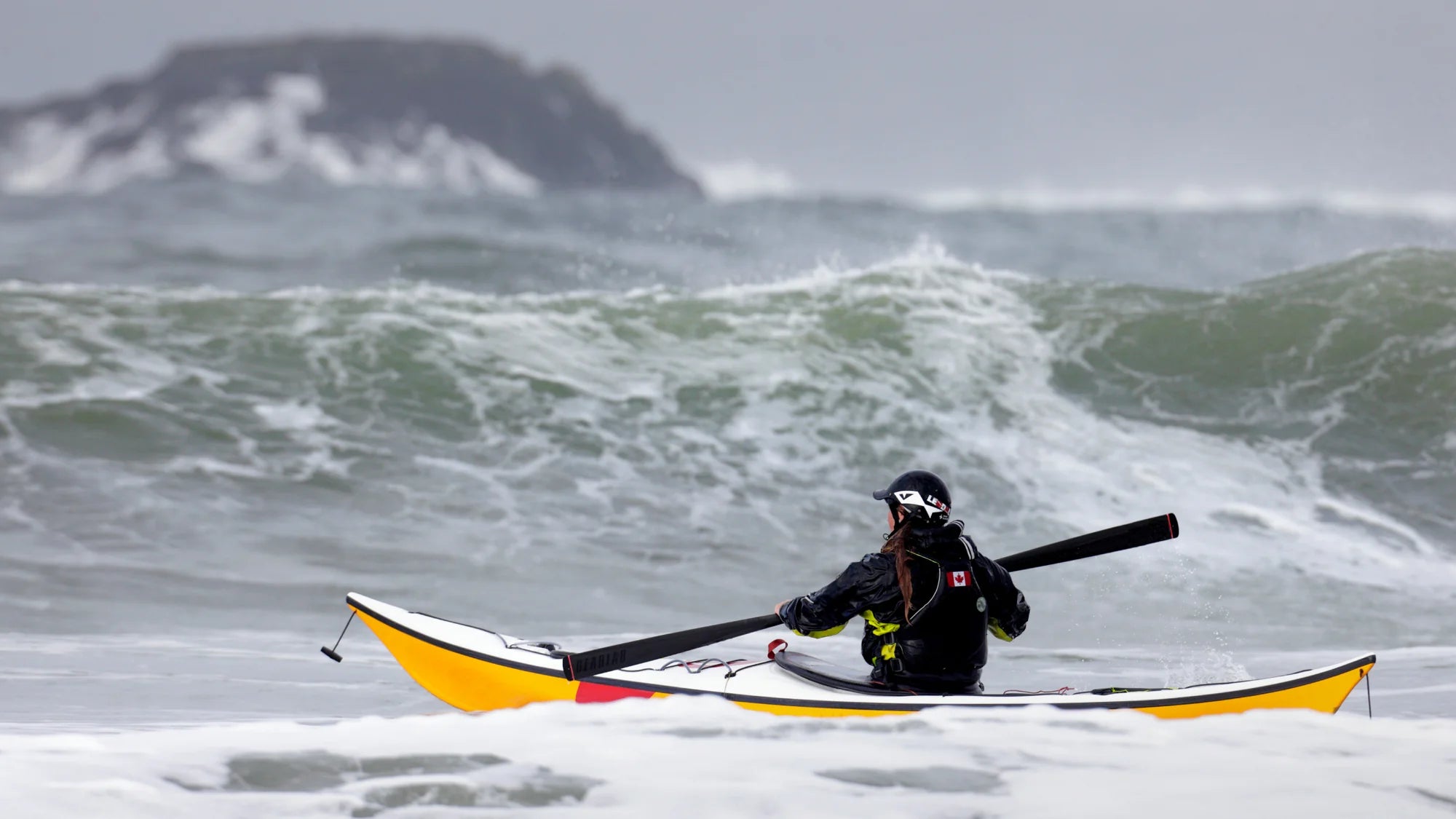 Person in a kayak on rough water with a helmet and paddle