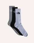 Three pairs of ribbed crew socks by The North Face, displayed in a fan arrangement on a solid taupe background. The socks are in heather gray, solid black, and solid white, each featuring the brand's logo on the cuff.