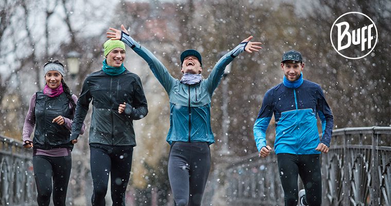 four people running in the snow wearing neckwarmers